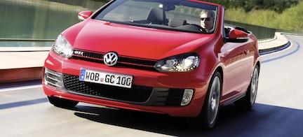 En röd Volkswagen Golf cabriolet kör längs en väg. (AI text)