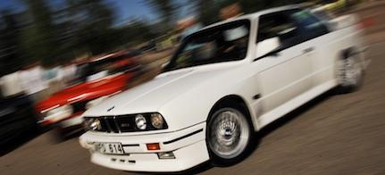 En vit BMW E30 M3 kör nedför vägen. (AI text)