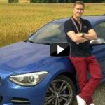 En man står bredvid en blå BMW M1. (AI text)