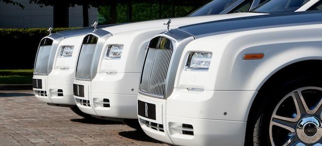 En grupp vita Rolls-Royce-limas parkerade framför ett byggnad. (AI text)