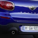 En blå Mini Cooper kör nerför en väg. (AI text)