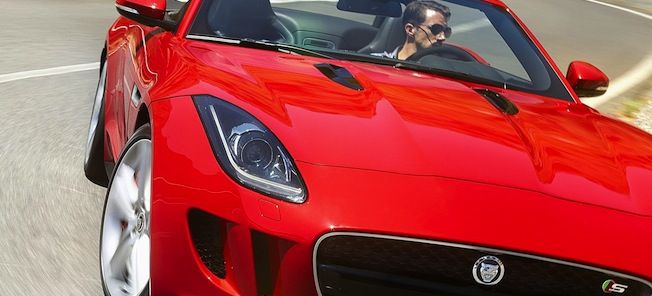En röd jaguar F-Type sportsbil kör längs en väg. (AI text)