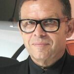 En man i glasögon står bredvid en bil. (AI text)