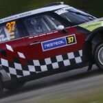 En Mini Cooper S rallybil kör ner en väg. (AI text)