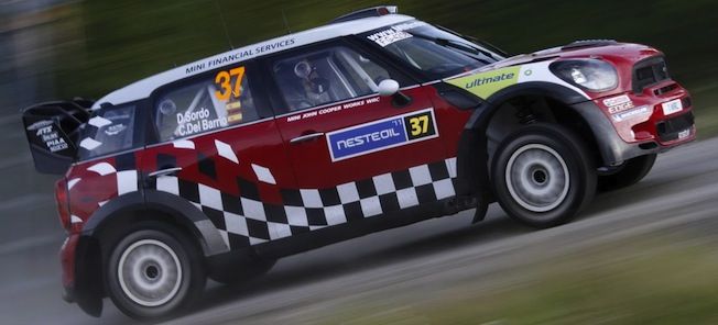 En Mini Cooper S rallybil kör ner en väg. (AI text)