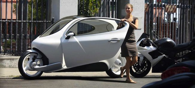 En kvinna står bredvid en motorcykel och en liten elbil. (AI text)