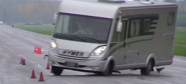 En campervan kör nedför en väg med koner i bakgrunden. (AI text)