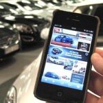 En person håller en mobiltelefon framför en bilstation. (AI text)