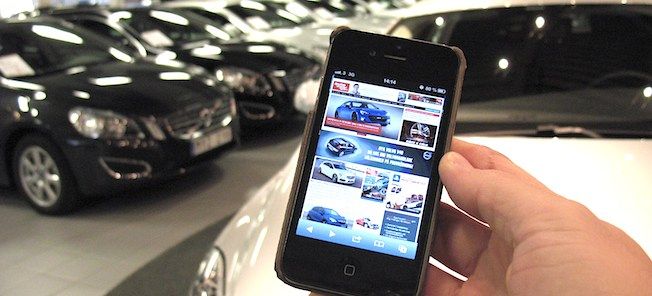 En person håller en mobiltelefon framför en bilstation. (AI text)