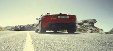 En röd jaguar F-Type cabriolet kör nedför en bergsväg. (AI text)