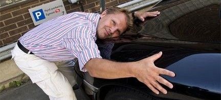 En man stödjer sig mot en bil. (AI text)