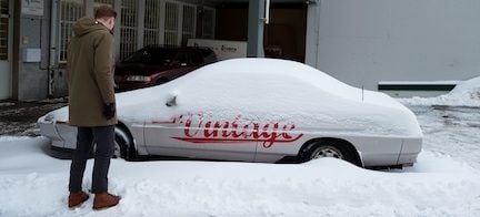 En man står bredvid en bil som är täckt av snö. (AI text)