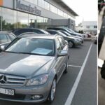 En man i kostym står bredvid en bil, intill honom står en annan man i kostym. (AI text)