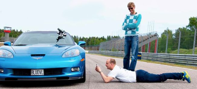 En man ligger på marken bredvid en blå Chevrolet Corvette Z06. (AI text)