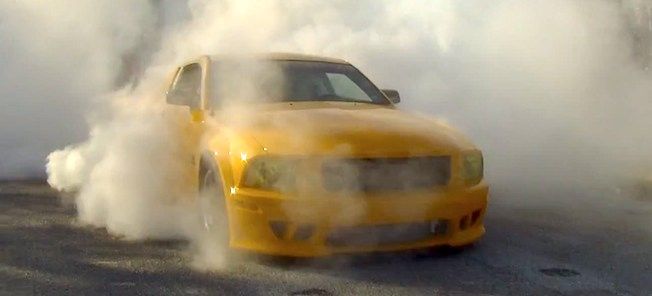 En gul bil kör nerför en gata med rök som kommer ut ifrån den. (AI text)