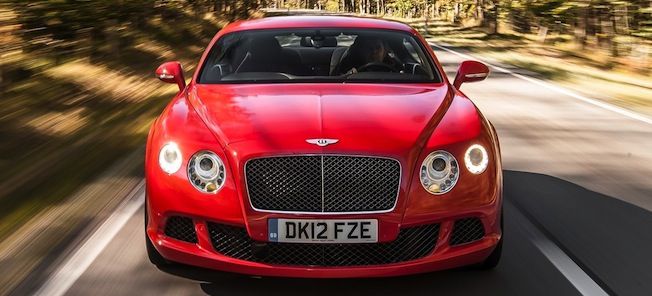 En röd Bentley Continental GT kör nerför en landsväg. (AI text)