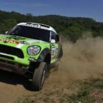 En grön Mini Cooper S kör nedför en grusväg. (AI text)