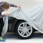 En man täcker en bil med en bilduk. (AI text)