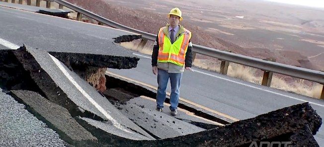 En arbetare står vid sidan av en väg som skadats av en jordras. (AI text)