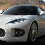 En man i kostym och slips står bredvid en sportbil. (AI text)