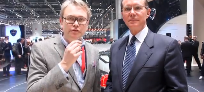 Två män i kostym står bredvid en bil. (AI text)