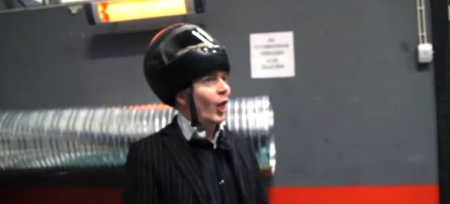 En man i kostym och hatt står i en parkeringsplats. (AI text)