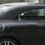 En svart cabriolejon parkerad framför ett byggnad. (AI text)