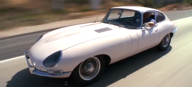 En klassisk Jaguar E-type kör nedför vägen. (AI text)