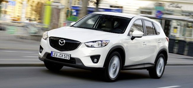 En vit Mazda CX-5 kör nedför en stadsgata. (AI text)
