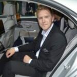 En man i kostym sitter i baksätet av en bil. (AI text)