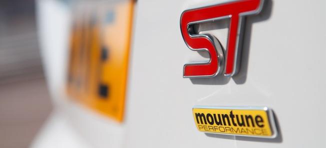 En vit bil med ett bergslogotyp på sidan. (AI text)