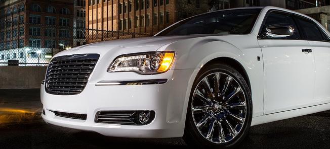 En vit Chrysler 300 står parkerad framför ett byggnad nattetid. (AI text)