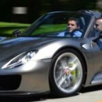 En silverfärgad Porsche Spyder kör längs en väg. (AI text)