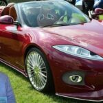 En man i kostym och slips står bredvid en röd sportbil. (AI text)