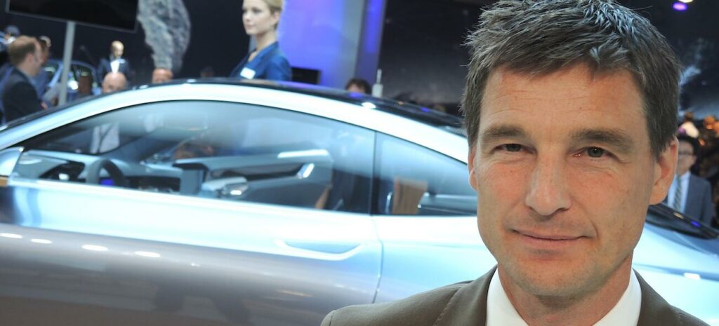 En man i kostym och slips står framför en bil. (AI text)