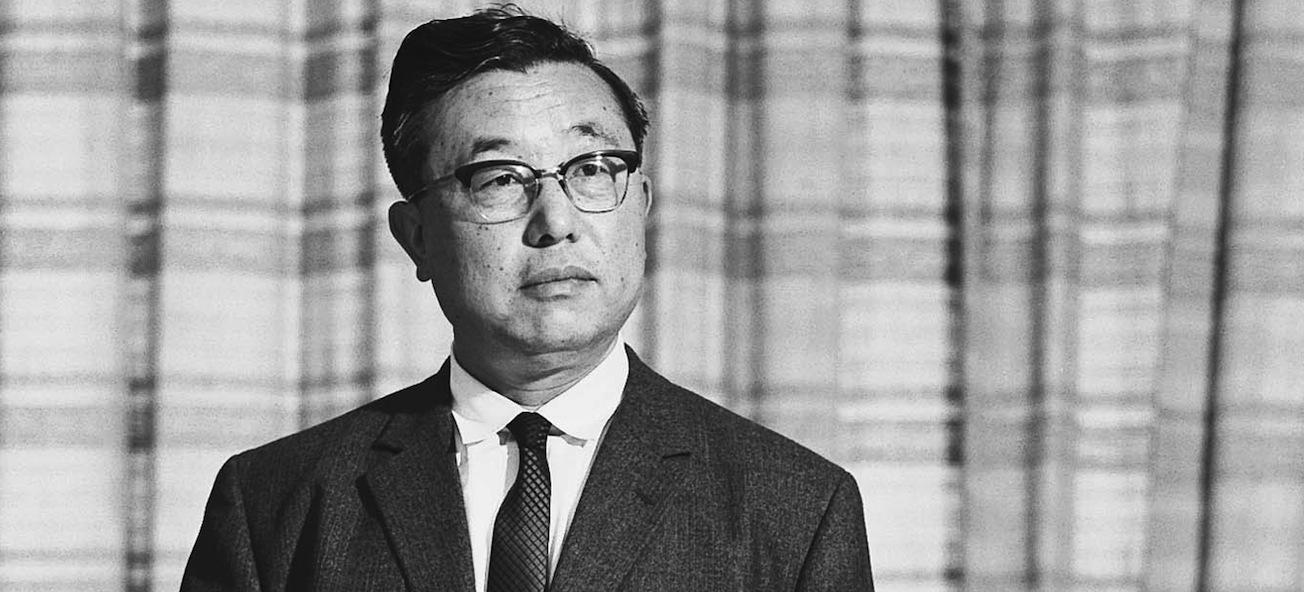 En man i kostym och slips står framför en gardin. (AI text)