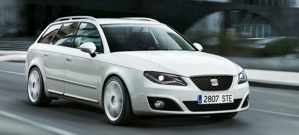 En vit bil körer nedför en stadsgata. (AI text)