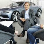 Tre män sitter i stolar och pratar om bilar. (AI text)