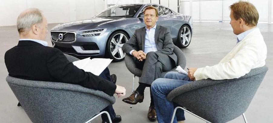 Tre män sitter i stolar och pratar om bilar. (AI text)