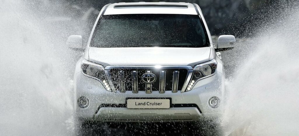 En vit Toyota Land Cruiser kör genom en vattenstråle. (AI text)