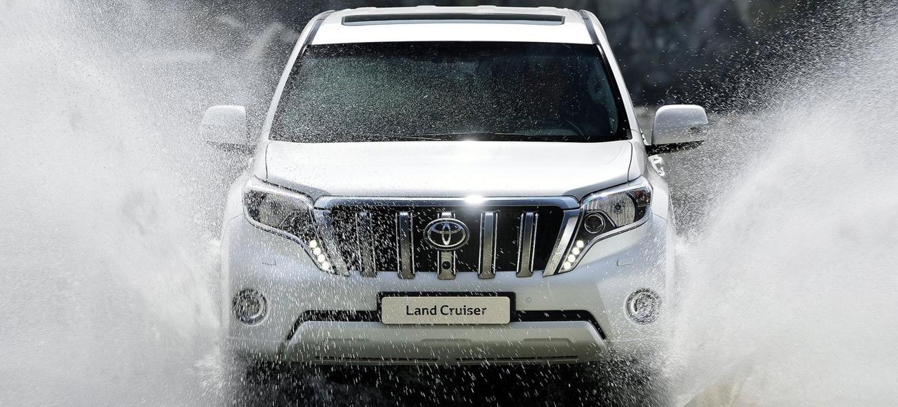 En vit Toyota Land Cruiser kör genom en vattenstråle. (AI text)