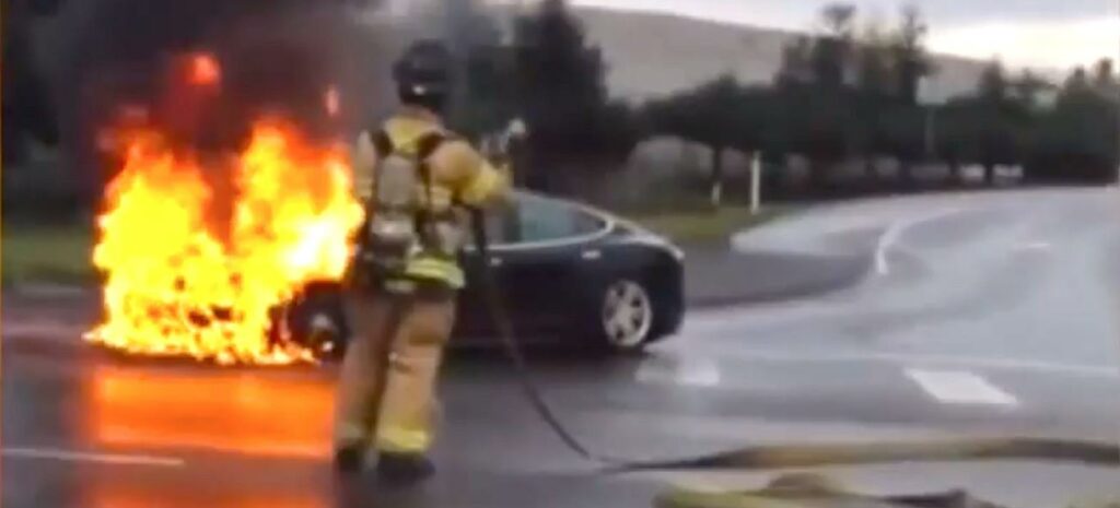 En brandman står bredvid en brinnande bil. (AI text)