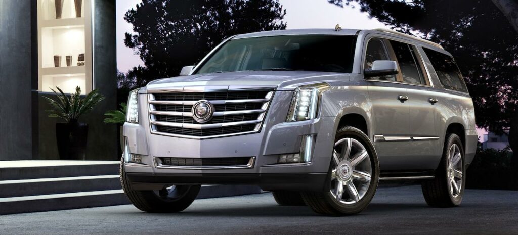 En silverfärgad Cadillac Escalade parkerad framför ett hus. (AI text)