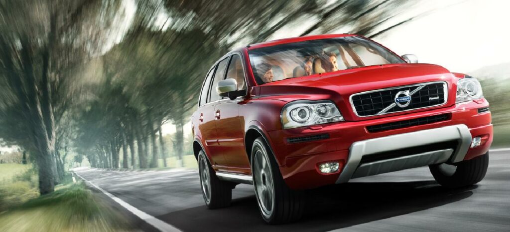 En röd Volvo XC90 kör längs en landsväg. (AI text)