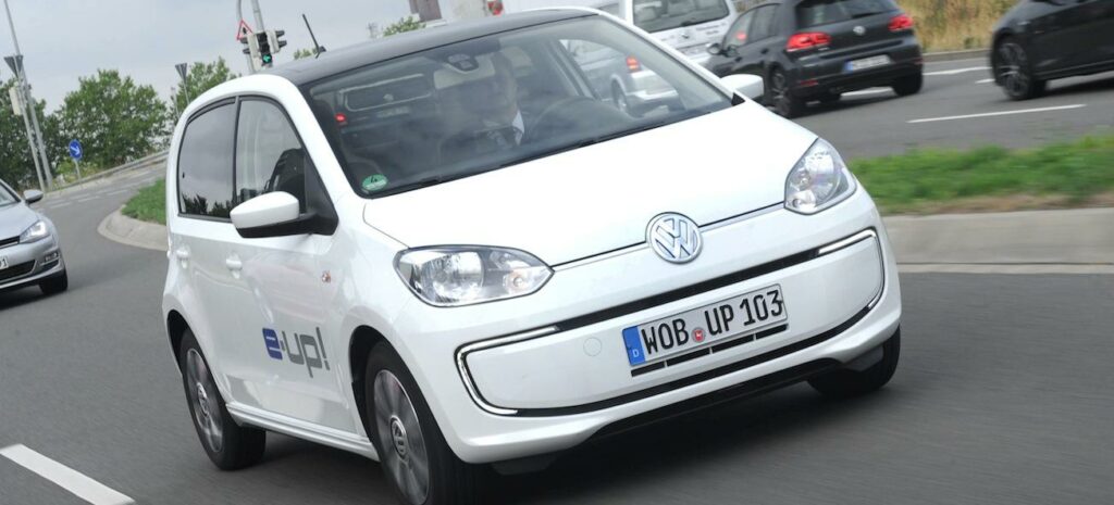En vit Volkswagen up! kör nedför en gata. (AI text)