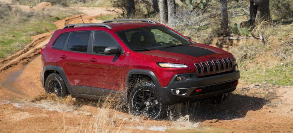 En röd Jeep Cherokee kör nerför en grusväg. (AI text)