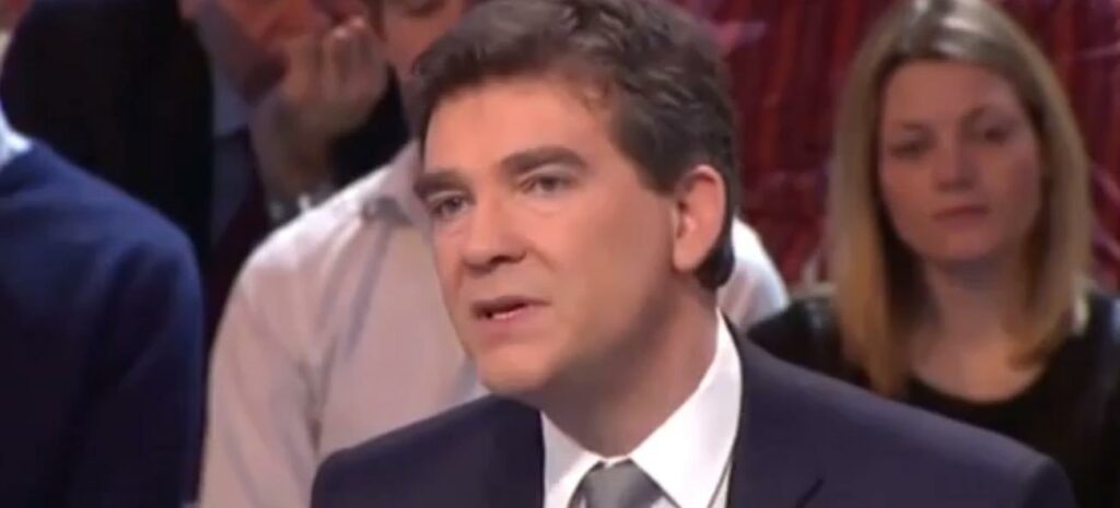 En man i kostym och slips talar inför en grupp människor. (AI text)