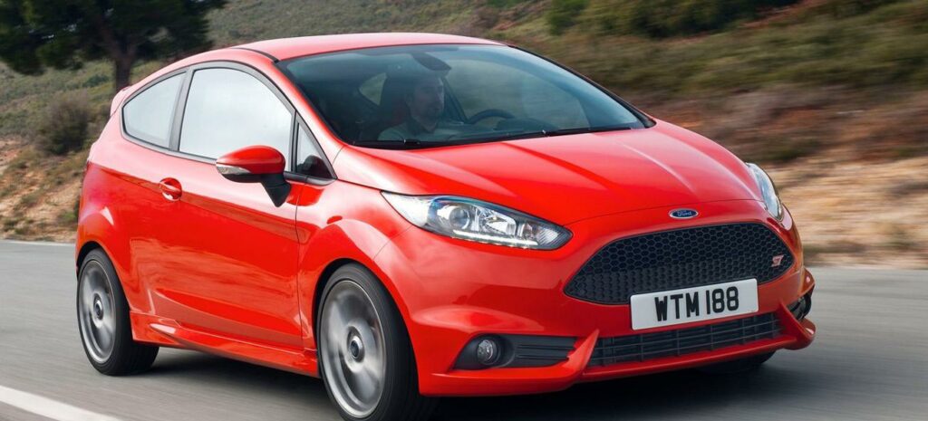 En röd Ford Fiesta kör längs en landsväg. (AI text)