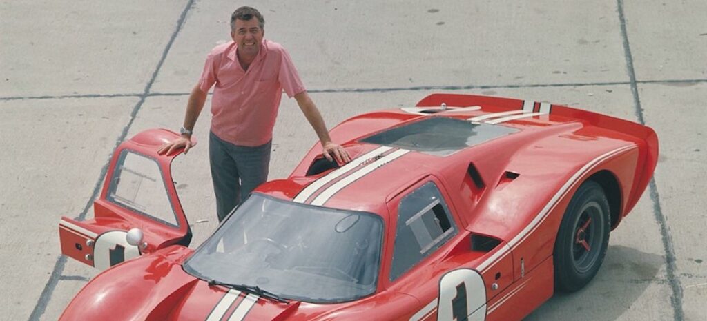 En man står bredvid en röd racebil. (AI text)