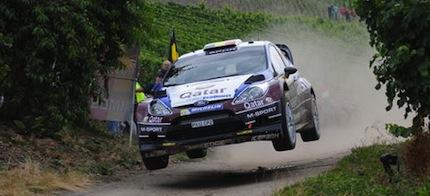 En rallybil hoppas över en grusväg. (AI text)